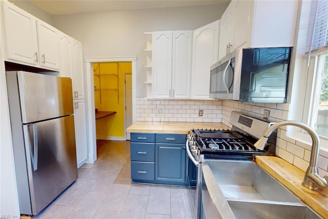 kitchen with butcher block countertops, stainless steel appliances, decorative backsplash, sink, and white cabinets