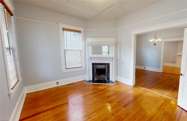 unfurnished living room with hardwood / wood-style flooring, a chandelier, and a tile fireplace