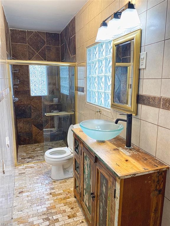 bathroom featuring toilet, vanity, a healthy amount of sunlight, and tile walls