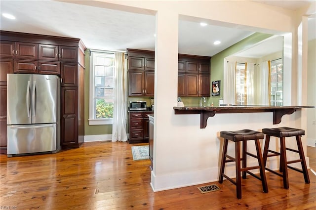 kitchen featuring stainless steel appliances, dark stone counters, light wood-type flooring, sink, and a breakfast bar area