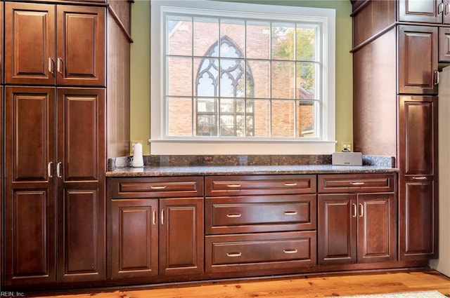 bar with dark stone countertops and light wood-type flooring