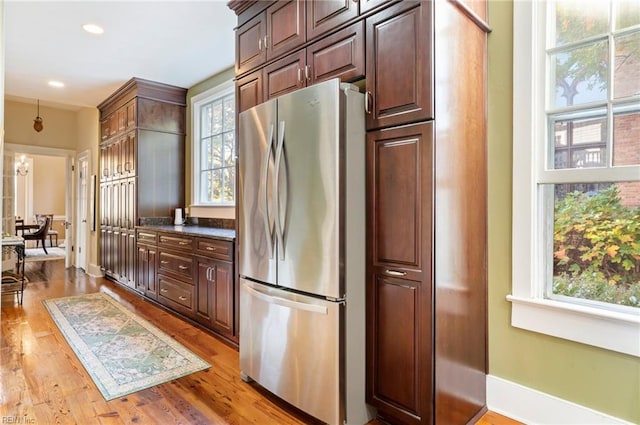 kitchen featuring dark stone counters, dark brown cabinetry, stainless steel refrigerator, and light hardwood / wood-style floors