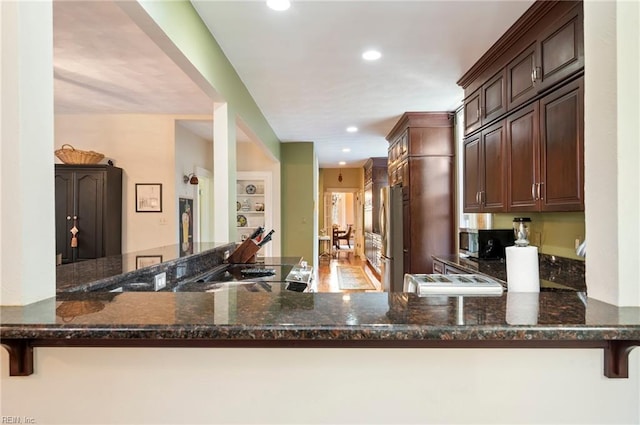 kitchen with dark stone counters, kitchen peninsula, dark brown cabinets, and stainless steel appliances