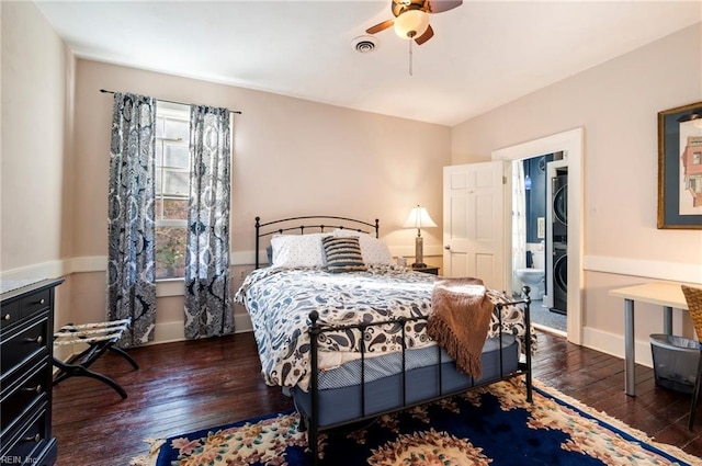 bedroom with dark wood-type flooring, ceiling fan, and stacked washer / dryer