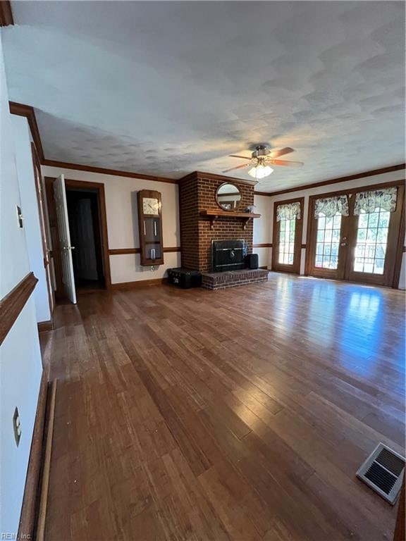 unfurnished living room with french doors, a fireplace, crown molding, dark wood-type flooring, and ceiling fan