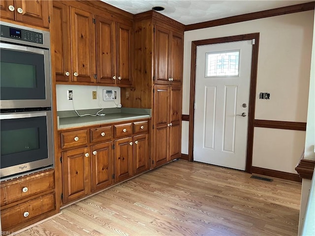 kitchen featuring stainless steel double oven, light hardwood / wood-style flooring, and ornamental molding