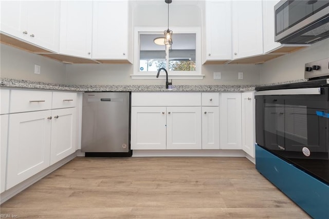 kitchen with light hardwood / wood-style floors, white cabinets, hanging light fixtures, light stone countertops, and appliances with stainless steel finishes