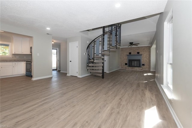 unfurnished living room with a brick fireplace, light hardwood / wood-style flooring, a textured ceiling, and ceiling fan