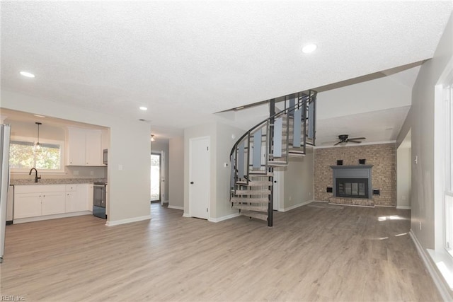 unfurnished living room with light wood-type flooring, a textured ceiling, and ceiling fan