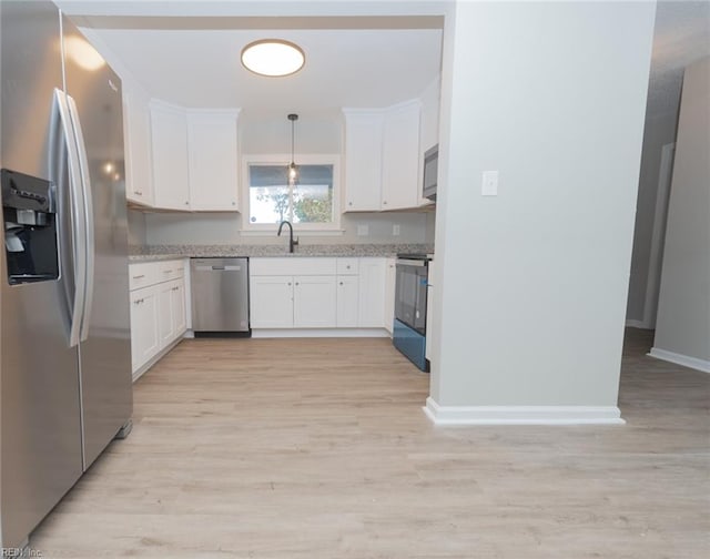 kitchen featuring stainless steel appliances, white cabinetry, sink, decorative light fixtures, and light wood-type flooring