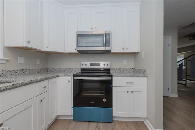 kitchen featuring white cabinets, light stone countertops, light wood-type flooring, and appliances with stainless steel finishes