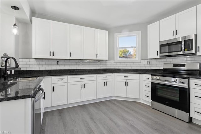 kitchen featuring stainless steel appliances, decorative light fixtures, sink, white cabinets, and light hardwood / wood-style flooring