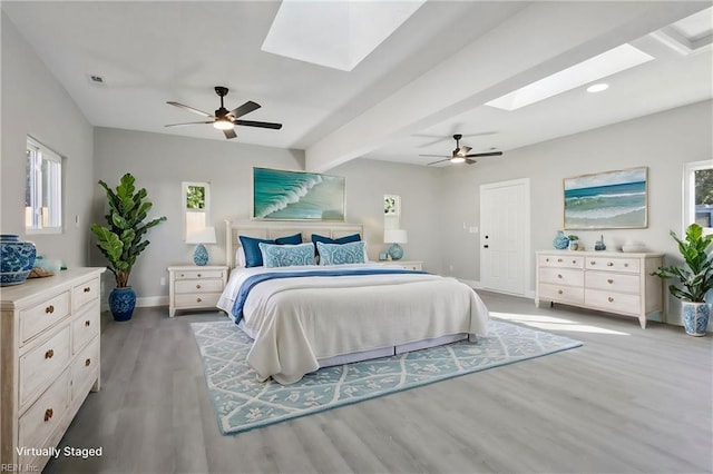 bedroom featuring ceiling fan, beamed ceiling, multiple windows, and light hardwood / wood-style flooring