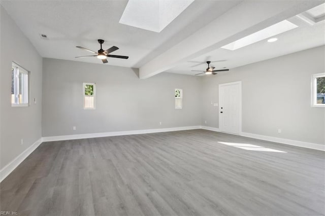 unfurnished room with ceiling fan, hardwood / wood-style flooring, beamed ceiling, and a skylight