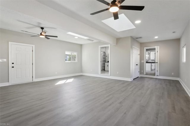 unfurnished living room featuring hardwood / wood-style floors, ceiling fan, a healthy amount of sunlight, and a skylight