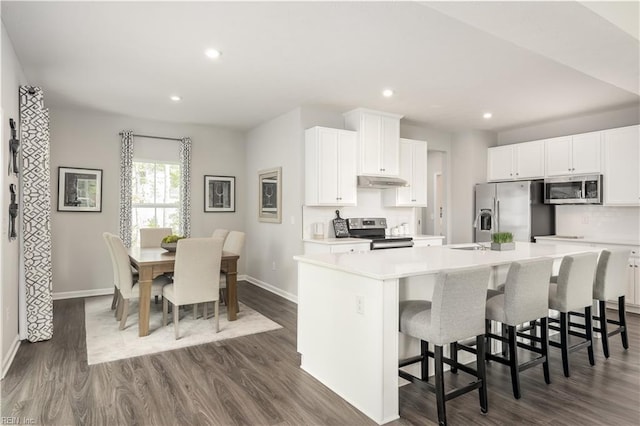 kitchen with white cabinetry, dark wood-type flooring, stainless steel appliances, a kitchen breakfast bar, and a center island with sink