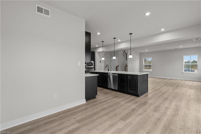 kitchen featuring appliances with stainless steel finishes, light wood-type flooring, a kitchen island with sink, sink, and pendant lighting