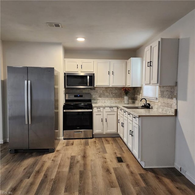 kitchen with white cabinets, appliances with stainless steel finishes, light hardwood / wood-style flooring, and sink