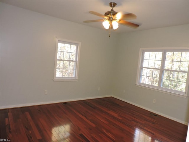 empty room with dark wood-type flooring, a wealth of natural light, and ceiling fan