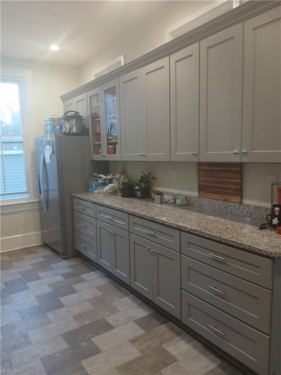 kitchen with stainless steel fridge, gray cabinetry, and light stone countertops