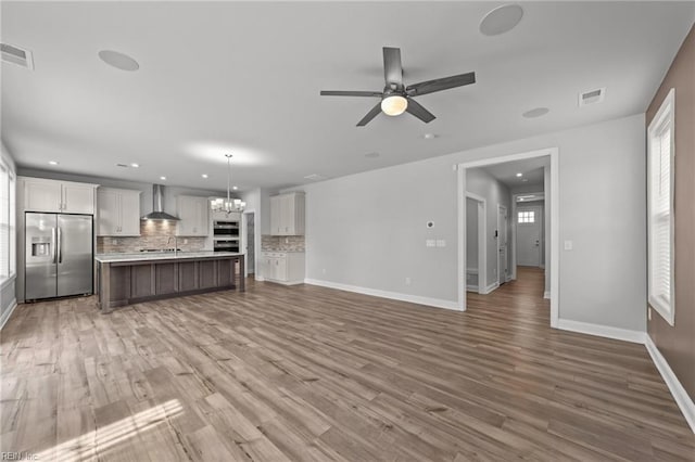 unfurnished living room featuring ceiling fan with notable chandelier and hardwood / wood-style flooring