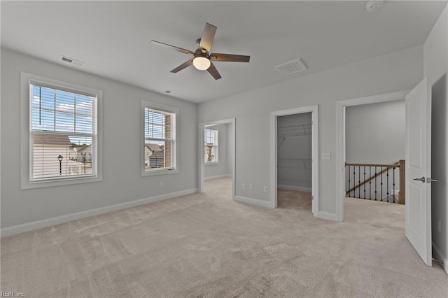 unfurnished bedroom with a closet, a walk in closet, light carpet, and ceiling fan