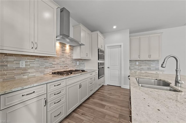 kitchen with white cabinetry, sink, light stone countertops, wall chimney range hood, and light wood-type flooring