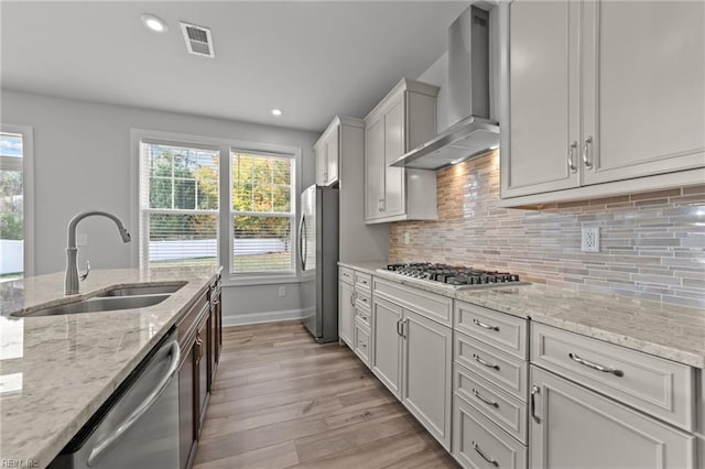 kitchen featuring stainless steel appliances, sink, wall chimney range hood, light stone countertops, and light hardwood / wood-style flooring