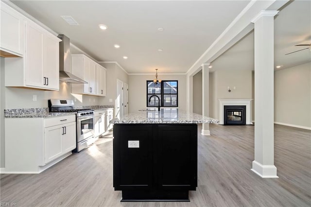 kitchen with stainless steel range with gas stovetop, white cabinetry, wall chimney exhaust hood, and a kitchen island with sink