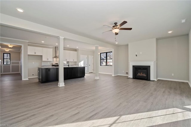 unfurnished living room featuring ornate columns, light hardwood / wood-style floors, ceiling fan, and sink