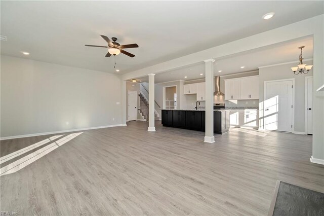 unfurnished living room featuring light hardwood / wood-style floors, ceiling fan with notable chandelier, sink, and decorative columns