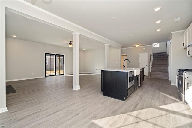 kitchen with light hardwood / wood-style floors, appliances with stainless steel finishes, ceiling fan, a kitchen island with sink, and white cabinets