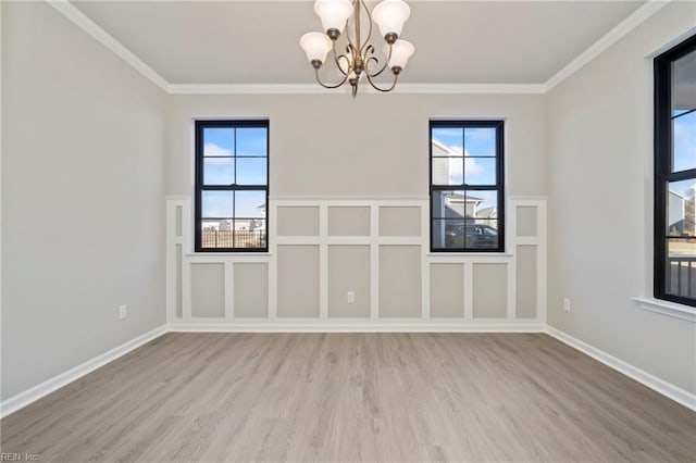 spare room with an inviting chandelier, hardwood / wood-style floors, ornamental molding, and plenty of natural light