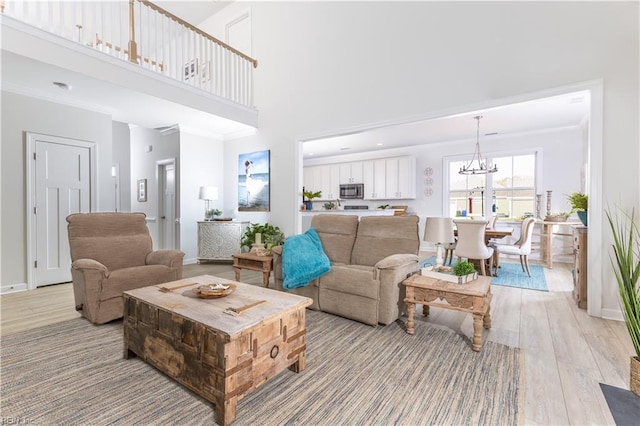 living room featuring a towering ceiling, a notable chandelier, crown molding, and light hardwood / wood-style flooring