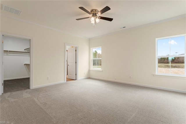 unfurnished bedroom with baseboards, visible vents, carpet floors, a walk in closet, and crown molding