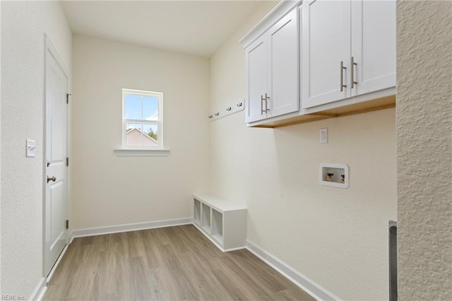 clothes washing area with baseboards, cabinet space, hookup for a washing machine, and light wood finished floors