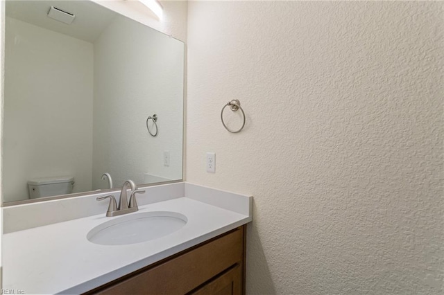 bathroom with toilet, vanity, and a textured wall