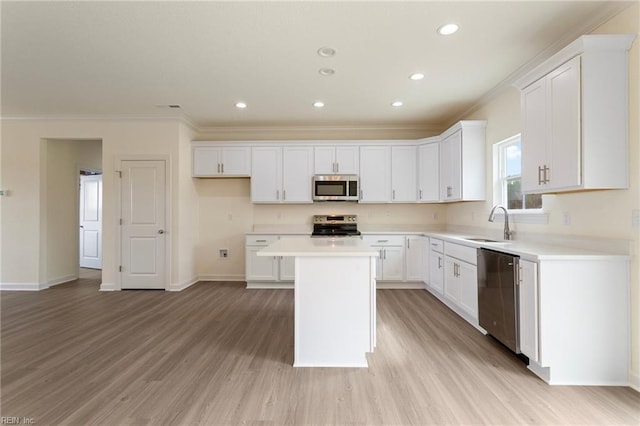 kitchen featuring a kitchen island, a sink, ornamental molding, stainless steel appliances, and white cabinetry