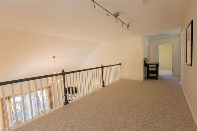 hallway with carpet, track lighting, and a notable chandelier