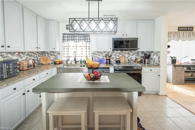 kitchen with tasteful backsplash, white cabinetry, appliances with stainless steel finishes, hanging light fixtures, and sink