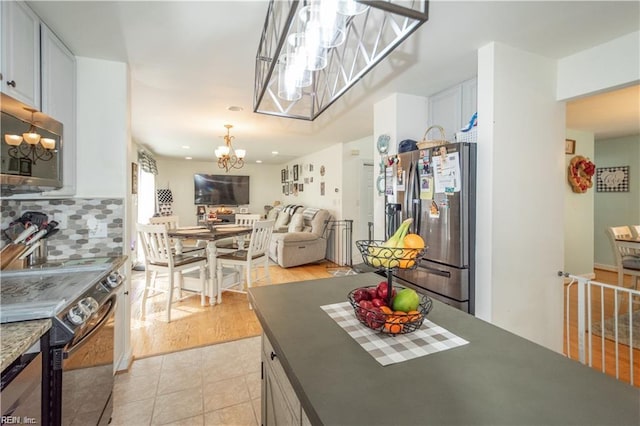 kitchen featuring stainless steel appliances, an inviting chandelier, white cabinets, backsplash, and light wood-type flooring