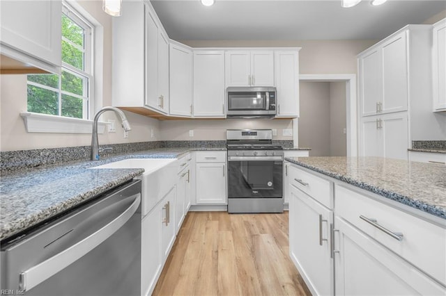 kitchen with stainless steel appliances, white cabinets, sink, and light hardwood / wood-style flooring