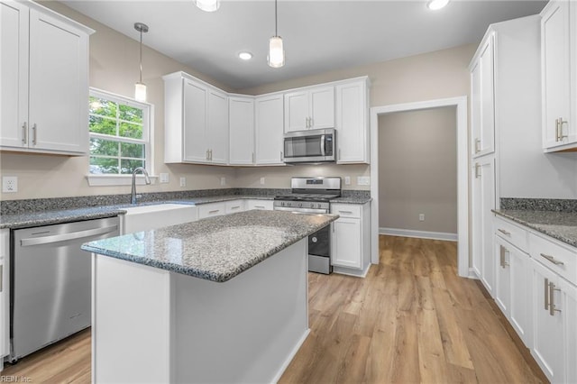 kitchen featuring light hardwood / wood-style floors, white cabinetry, light stone counters, appliances with stainless steel finishes, and a center island