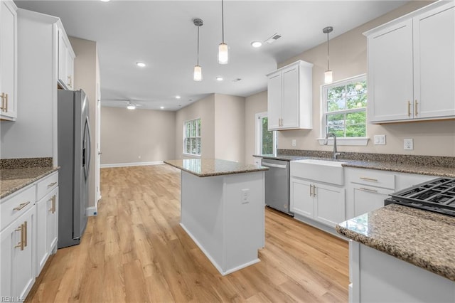 kitchen featuring light hardwood / wood-style flooring, a kitchen island, white cabinetry, appliances with stainless steel finishes, and decorative light fixtures