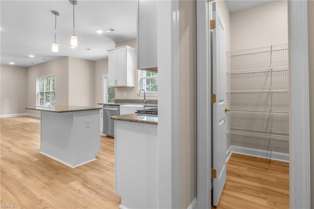 kitchen with a kitchen island, light wood-type flooring, a healthy amount of sunlight, and white cabinets