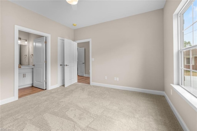 unfurnished bedroom featuring ceiling fan, light colored carpet, multiple windows, and connected bathroom