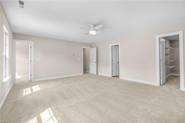 unfurnished bedroom with a closet, a spacious closet, light colored carpet, and ceiling fan