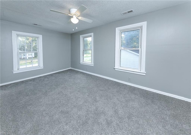 spare room with a textured ceiling, dark colored carpet, ceiling fan, and plenty of natural light