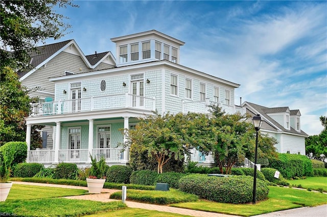 view of front of house with covered porch, a balcony, and a front lawn