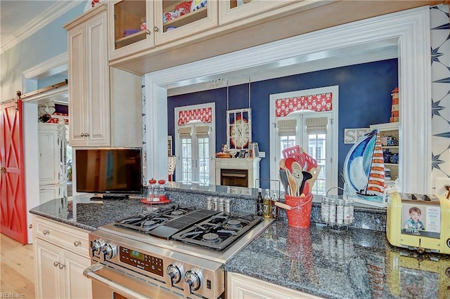 kitchen featuring stainless steel stove, crown molding, light wood-type flooring, decorative light fixtures, and dark stone countertops